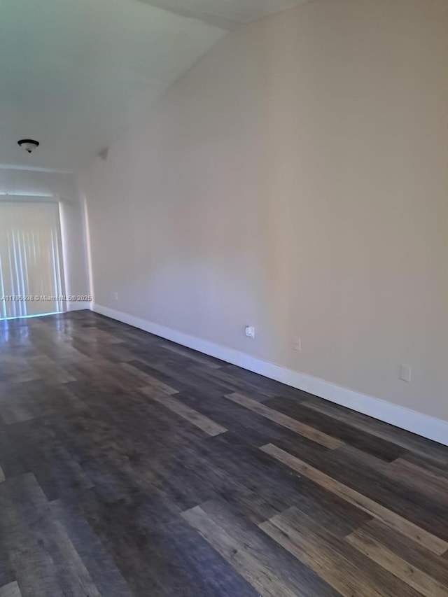 empty room featuring baseboards, dark wood-style floors, and vaulted ceiling