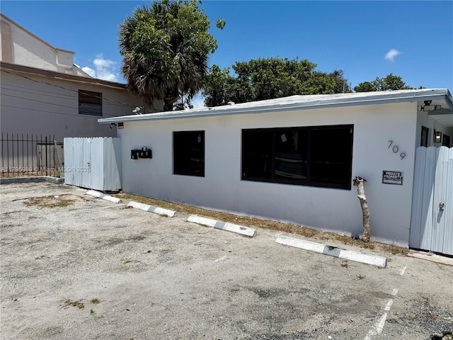 rear view of house featuring fence, stucco siding, and uncovered parking