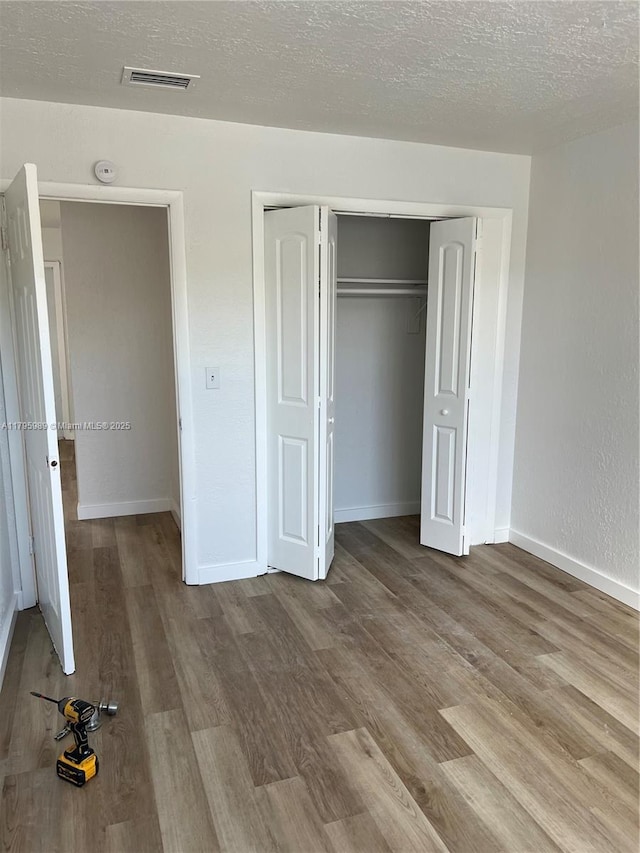 unfurnished bedroom featuring a textured ceiling, visible vents, wood finished floors, baseboards, and a closet