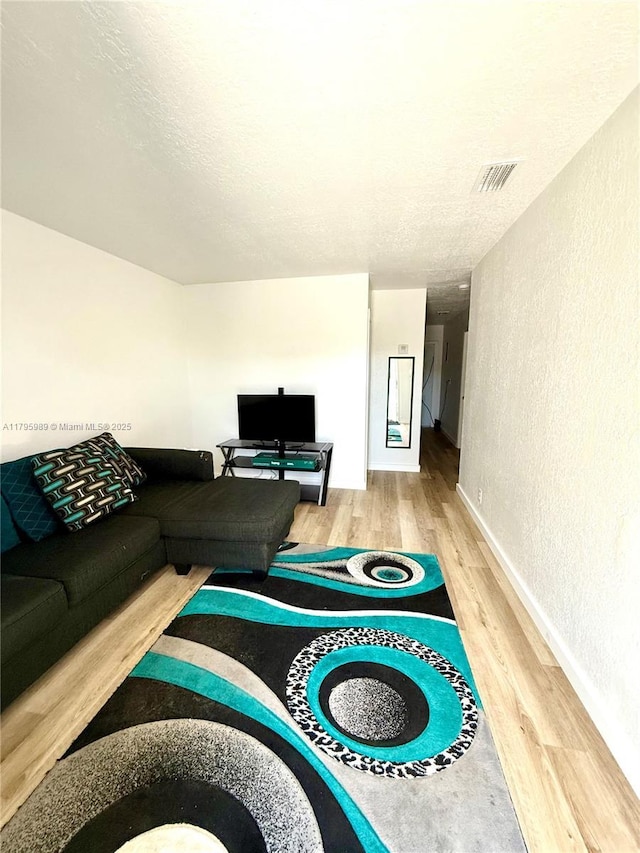 living room featuring visible vents, a textured wall, wood finished floors, baseboards, and a textured ceiling