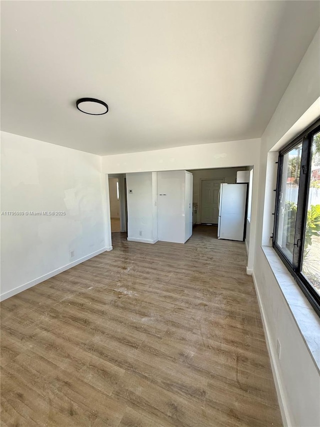 unfurnished bedroom featuring baseboards, freestanding refrigerator, and wood finished floors