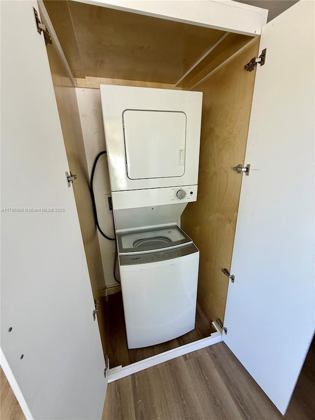 laundry area with stacked washer / drying machine and wood finished floors