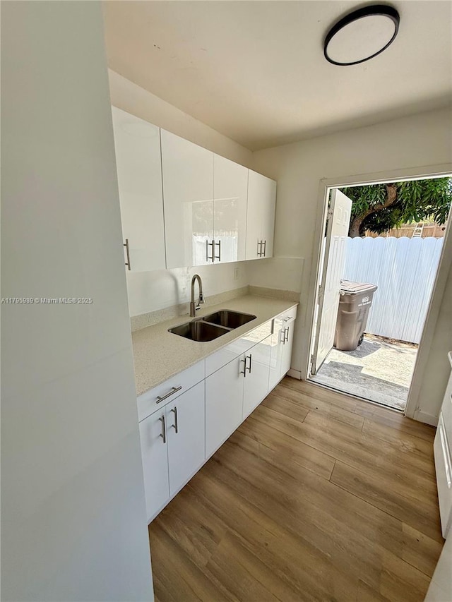 kitchen with wood finished floors, modern cabinets, light countertops, white cabinets, and a sink