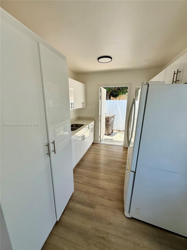 709 13th St, West Palm Beach, FL 33401 - kitchen with freestanding refrigerator, white cabinetry, wood finished floors, light countertops, and a sink