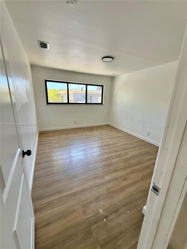 unfurnished room featuring baseboards, visible vents, and wood finished floors