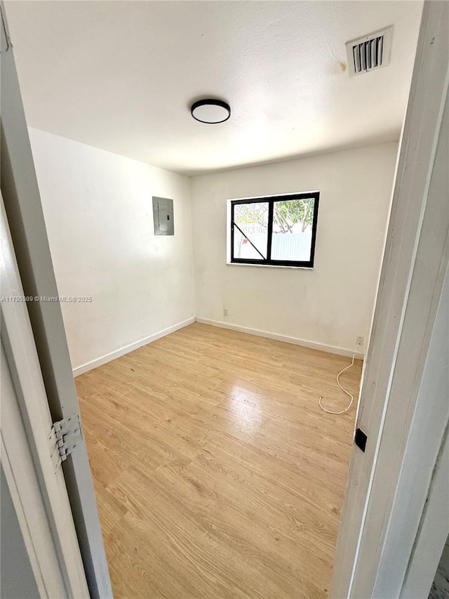 spare room featuring baseboards, electric panel, wood finished floors, and visible vents
