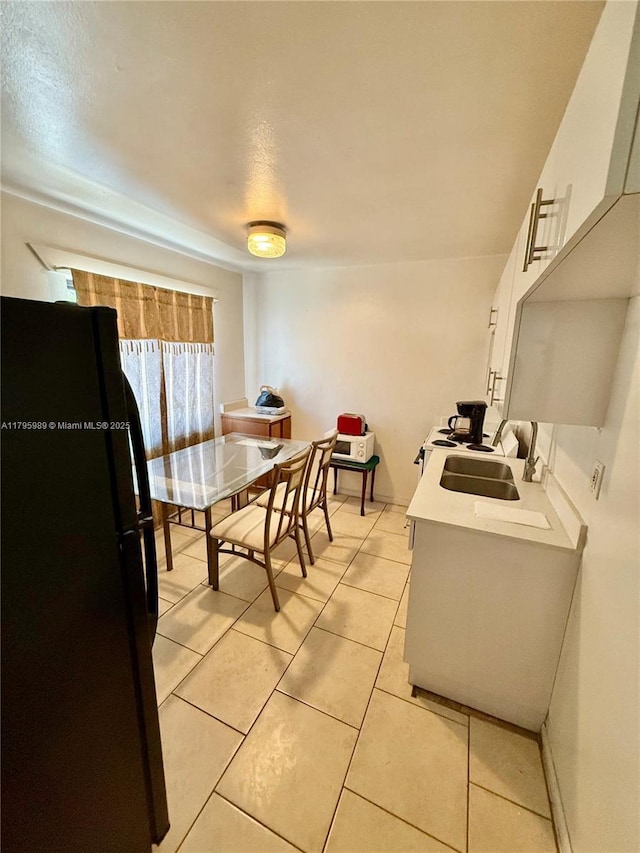 kitchen featuring a sink, light countertops, freestanding refrigerator, white cabinetry, and light tile patterned floors
