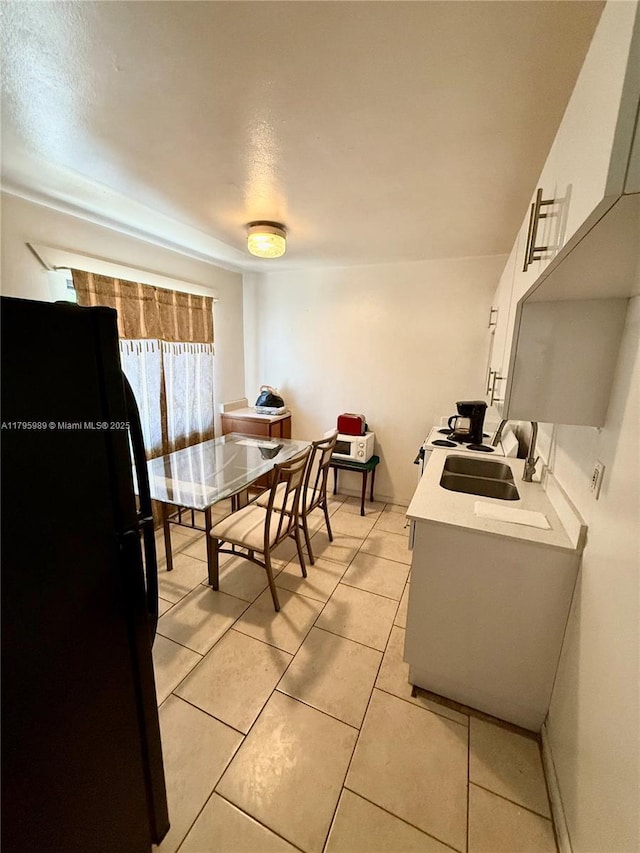 kitchen with freestanding refrigerator, light countertops, white cabinetry, a sink, and light tile patterned floors