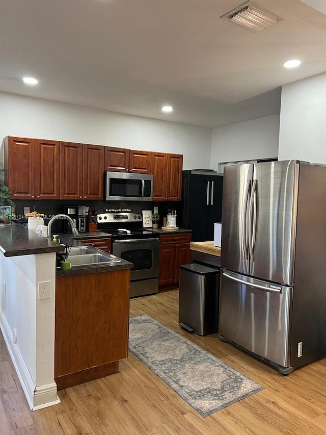 kitchen featuring visible vents, dark countertops, light wood-type flooring, a sink, and appliances with stainless steel finishes