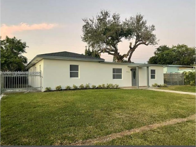 ranch-style house with a lawn, fence, and stucco siding
