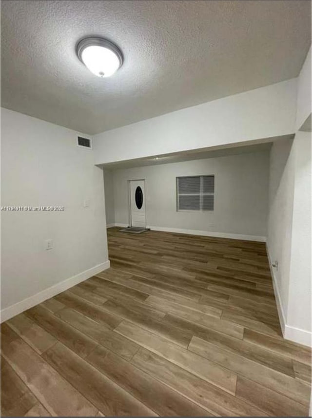 finished basement with wood finished floors, baseboards, a textured ceiling, and visible vents