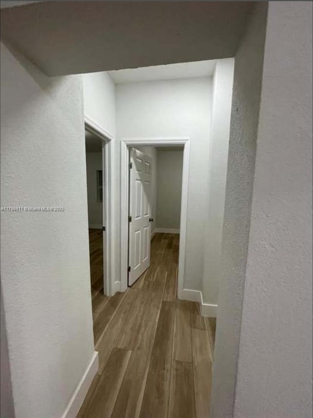 hall featuring baseboards, a textured wall, and wood finished floors