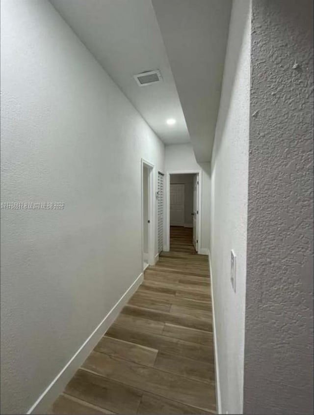 hall with baseboards, a textured wall, recessed lighting, and wood finished floors