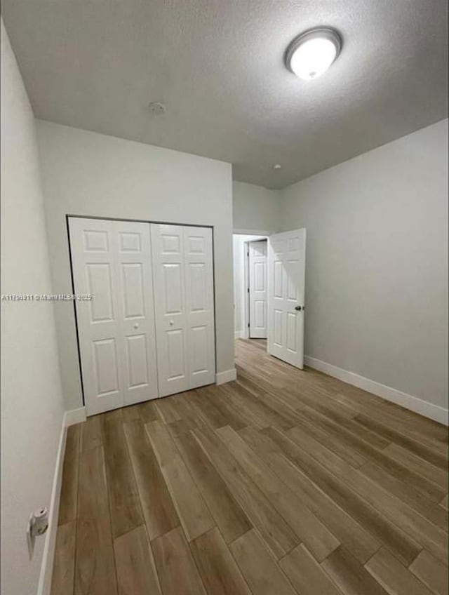unfurnished bedroom featuring a textured ceiling, baseboards, a closet, and wood finished floors