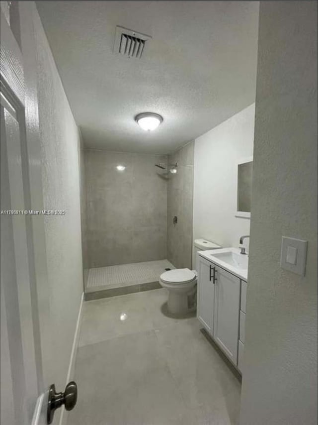 full bathroom featuring toilet, a textured wall, visible vents, and tiled shower