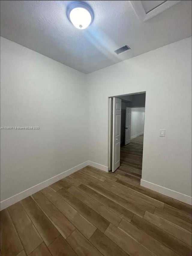 unfurnished room with baseboards, dark wood-style flooring, and visible vents