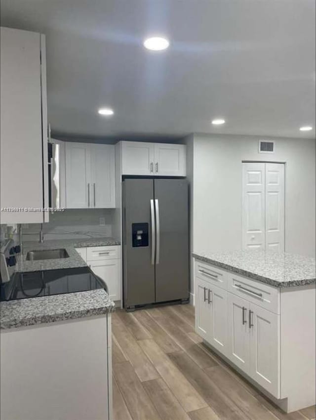 kitchen featuring recessed lighting, light stone counters, and stainless steel fridge