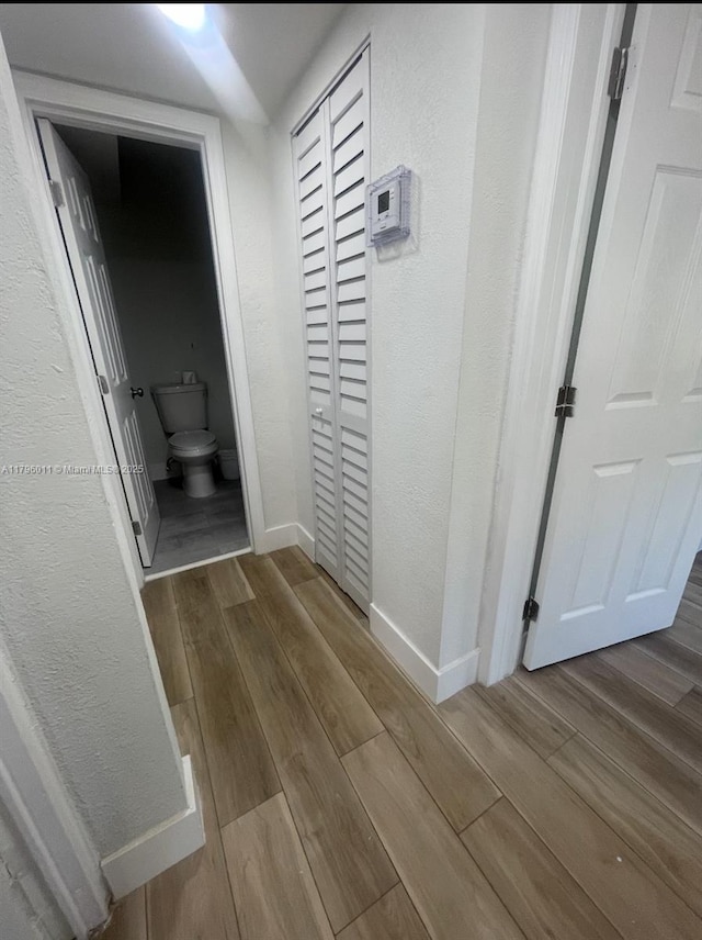 hall featuring baseboards, a textured wall, and wood finished floors