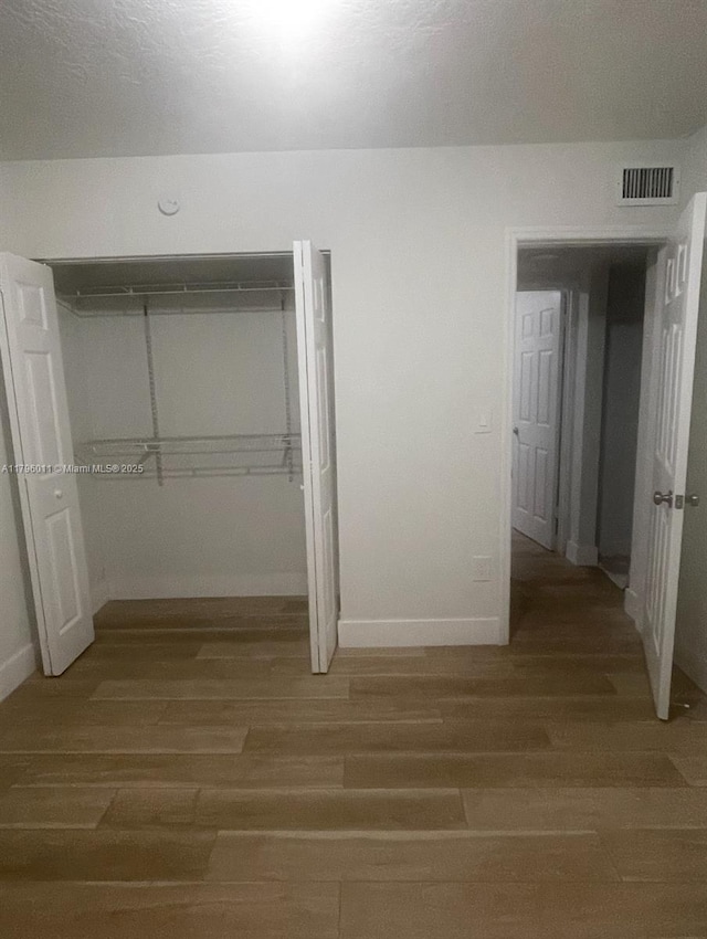unfurnished bedroom featuring baseboards, visible vents, wood finished floors, and a closet
