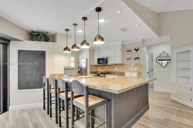 kitchen with stainless steel appliances, decorative backsplash, a breakfast bar, white cabinets, and light wood finished floors
