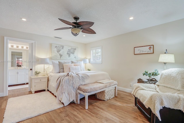 bedroom featuring a textured ceiling, light wood-type flooring, baseboards, ensuite bathroom, and ceiling fan