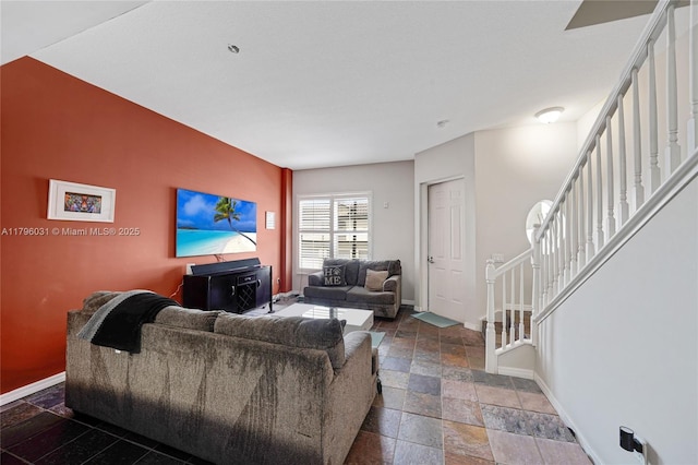 living area with baseboards, stone tile floors, and stairway