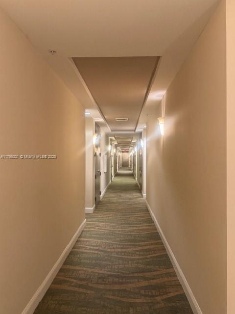 hallway featuring baseboards and dark colored carpet