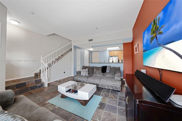 living room featuring stone tile flooring, stairway, and baseboards