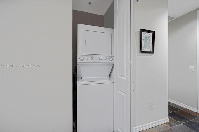 clothes washing area featuring estacked washer and dryer, baseboards, and stone tile flooring