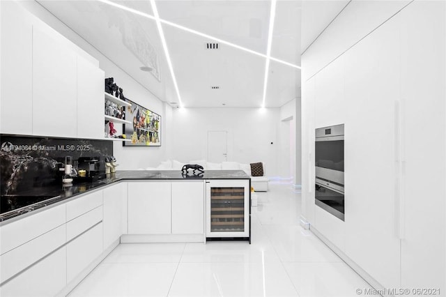 kitchen with a peninsula, wine cooler, dark countertops, white cabinetry, and light tile patterned floors