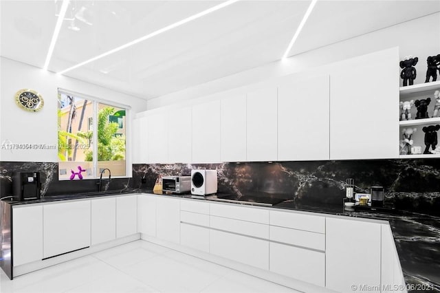 kitchen featuring white cabinets, dark countertops, a sink, decorative backsplash, and modern cabinets