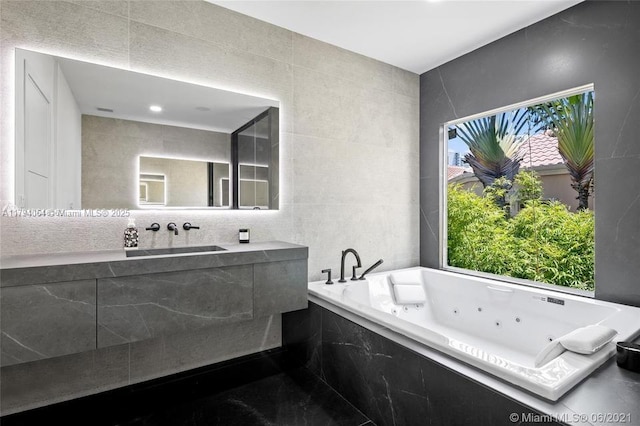 bathroom with tile walls, vanity, and a tub with jets