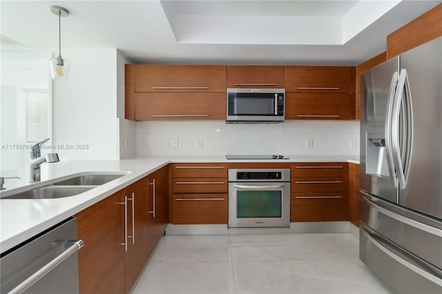 kitchen with a tray ceiling, brown cabinetry, stainless steel appliances, and a sink