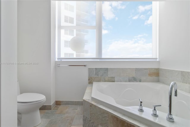 bathroom with a garden tub, toilet, baseboards, and stone finish floor