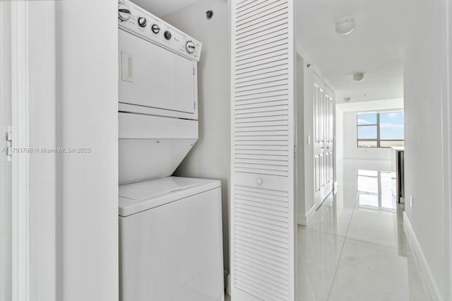 laundry room featuring laundry area, stacked washer and dryer, baseboards, and light tile patterned floors