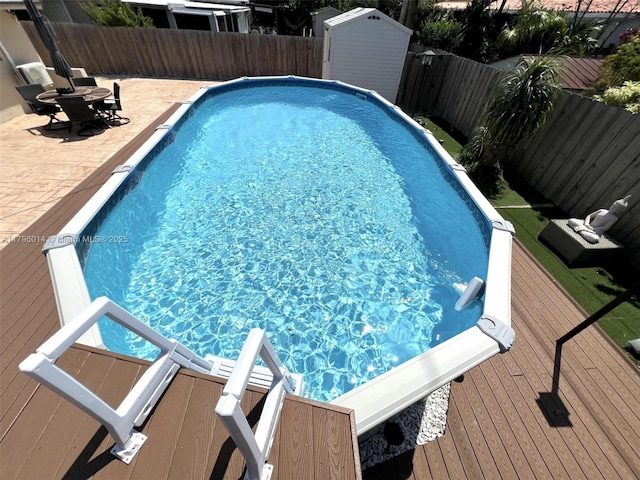 view of pool with a shed, a deck, a fenced backyard, a fenced in pool, and a patio