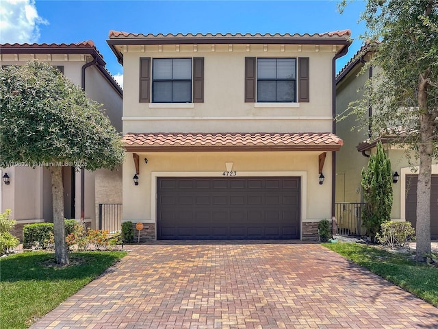 mediterranean / spanish house featuring a tile roof, decorative driveway, an attached garage, stone siding, and stucco siding