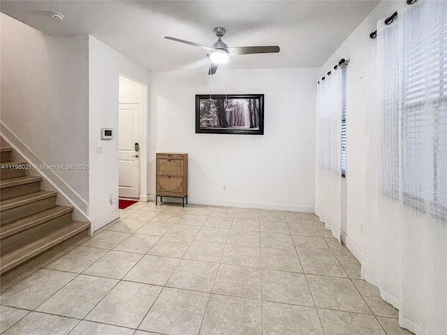 empty room featuring a ceiling fan, baseboards, light tile patterned floors, and stairway