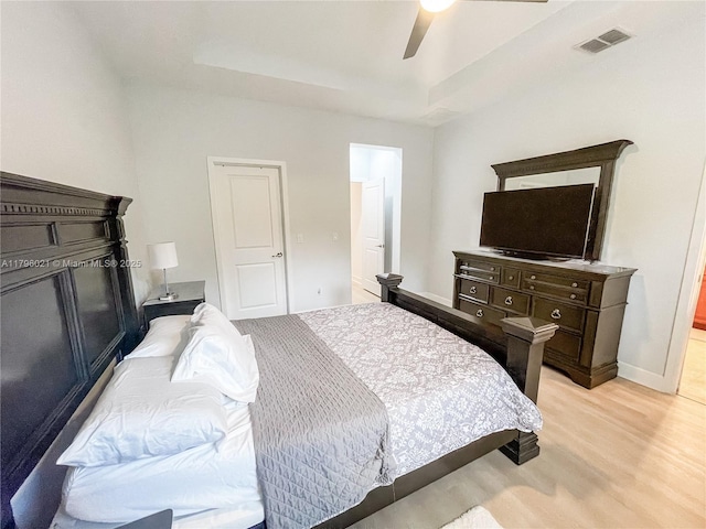 bedroom featuring a raised ceiling, light wood-style flooring, a ceiling fan, baseboards, and visible vents