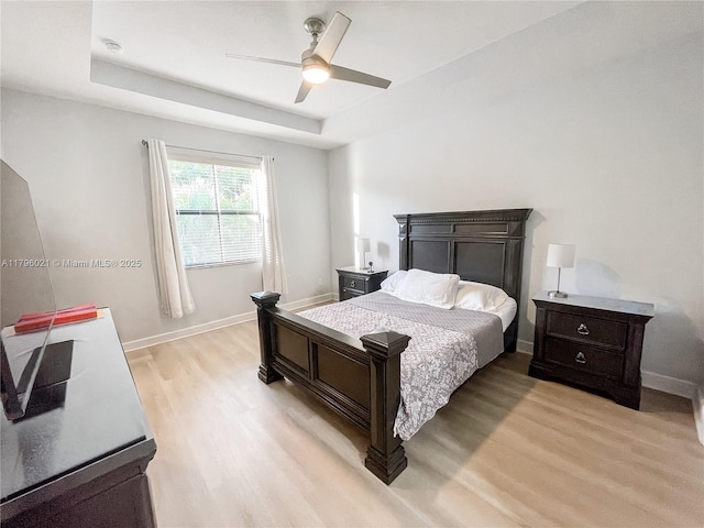 bedroom featuring baseboards, light wood finished floors, ceiling fan, and a tray ceiling