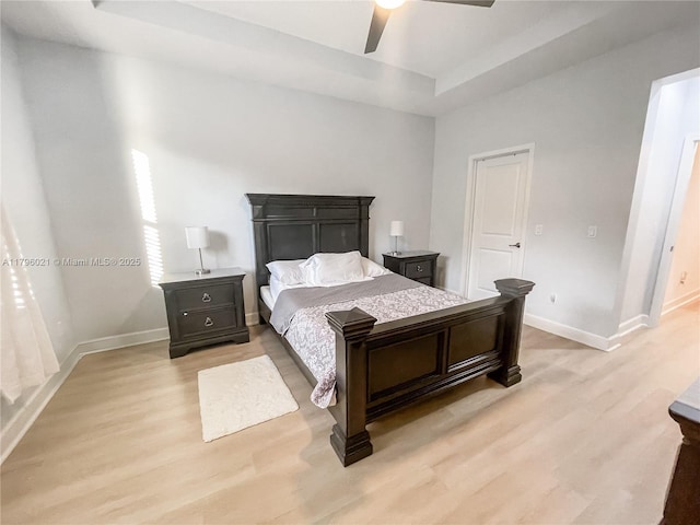 bedroom featuring light wood-style floors, a ceiling fan, baseboards, and a tray ceiling