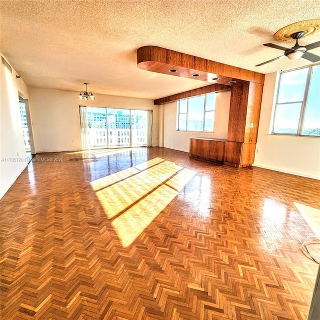 empty room featuring a textured ceiling, a healthy amount of sunlight, and ceiling fan with notable chandelier
