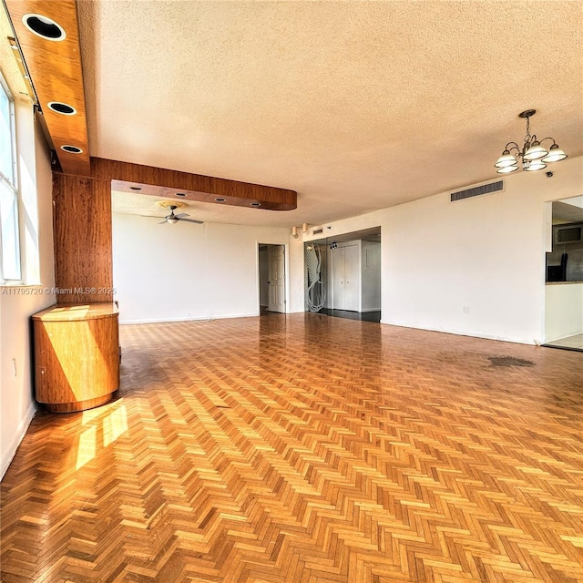 unfurnished room featuring visible vents, a textured ceiling, ceiling fan with notable chandelier, and baseboards