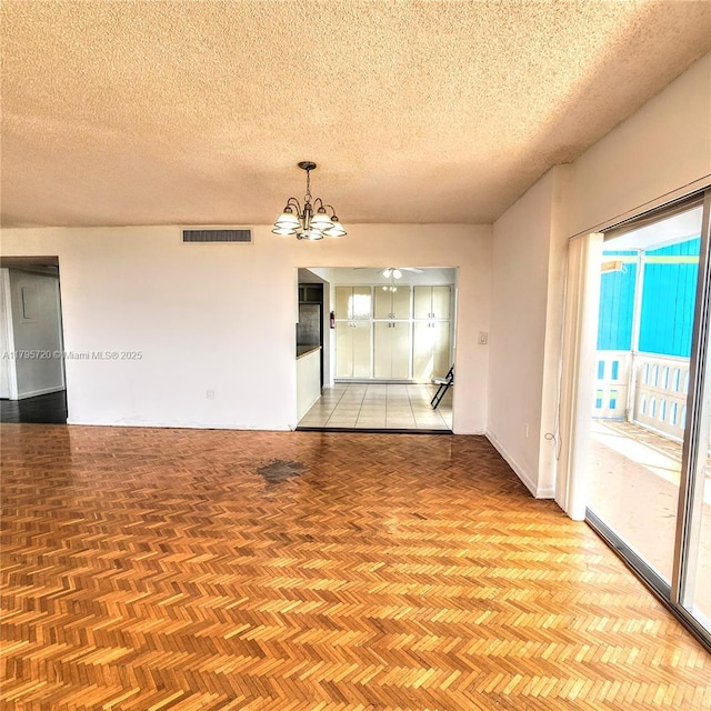 spare room with a chandelier, a textured ceiling, visible vents, and baseboards