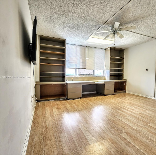 unfurnished living room with a textured ceiling, ceiling fan, built in study area, and light wood-style floors