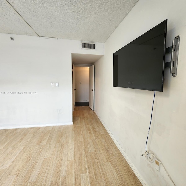 unfurnished room featuring baseboards, light wood-type flooring, a textured ceiling, and visible vents