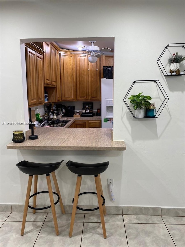 kitchen with a kitchen breakfast bar, light tile patterned floors, light countertops, a peninsula, and white fridge with ice dispenser