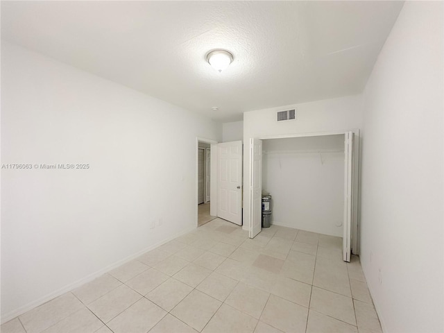 unfurnished bedroom featuring a textured ceiling, visible vents, light tile patterned floors, and a closet