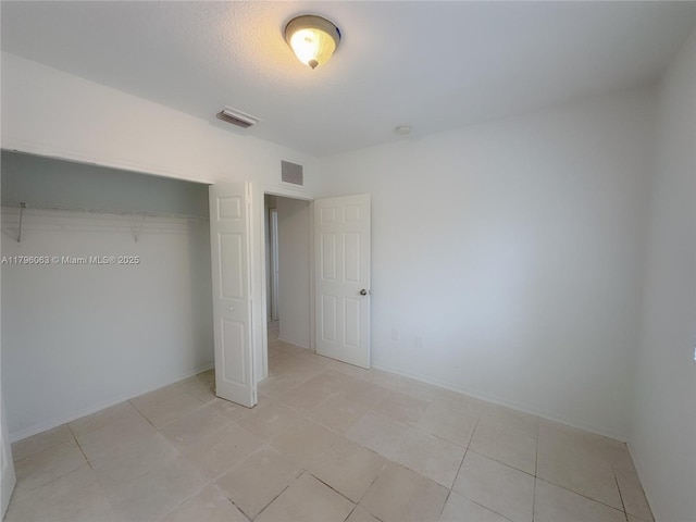 unfurnished bedroom featuring light tile patterned flooring, baseboards, visible vents, and a closet