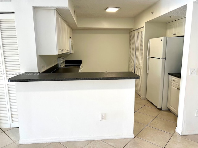 kitchen with light tile patterned floors, dark countertops, a peninsula, and white appliances